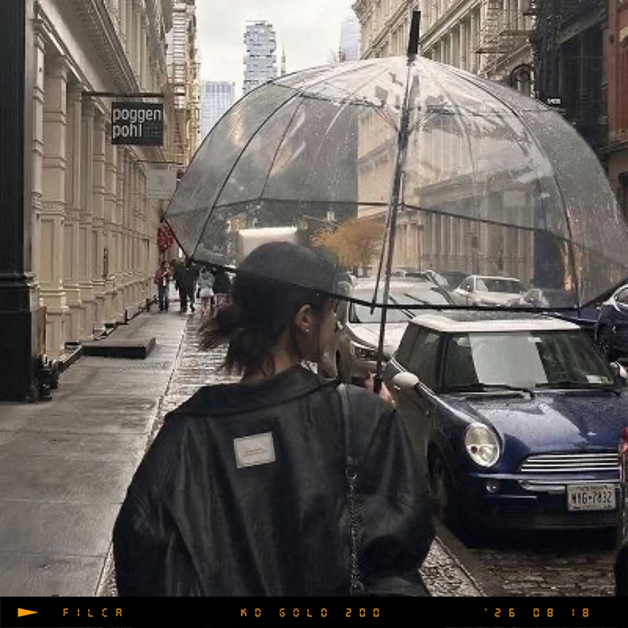 A woman with a clear umbrella on a rainy street, with a film-edge data bar