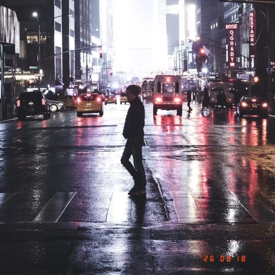 A rain-soaked city crossing at night with an orange LED date stamp