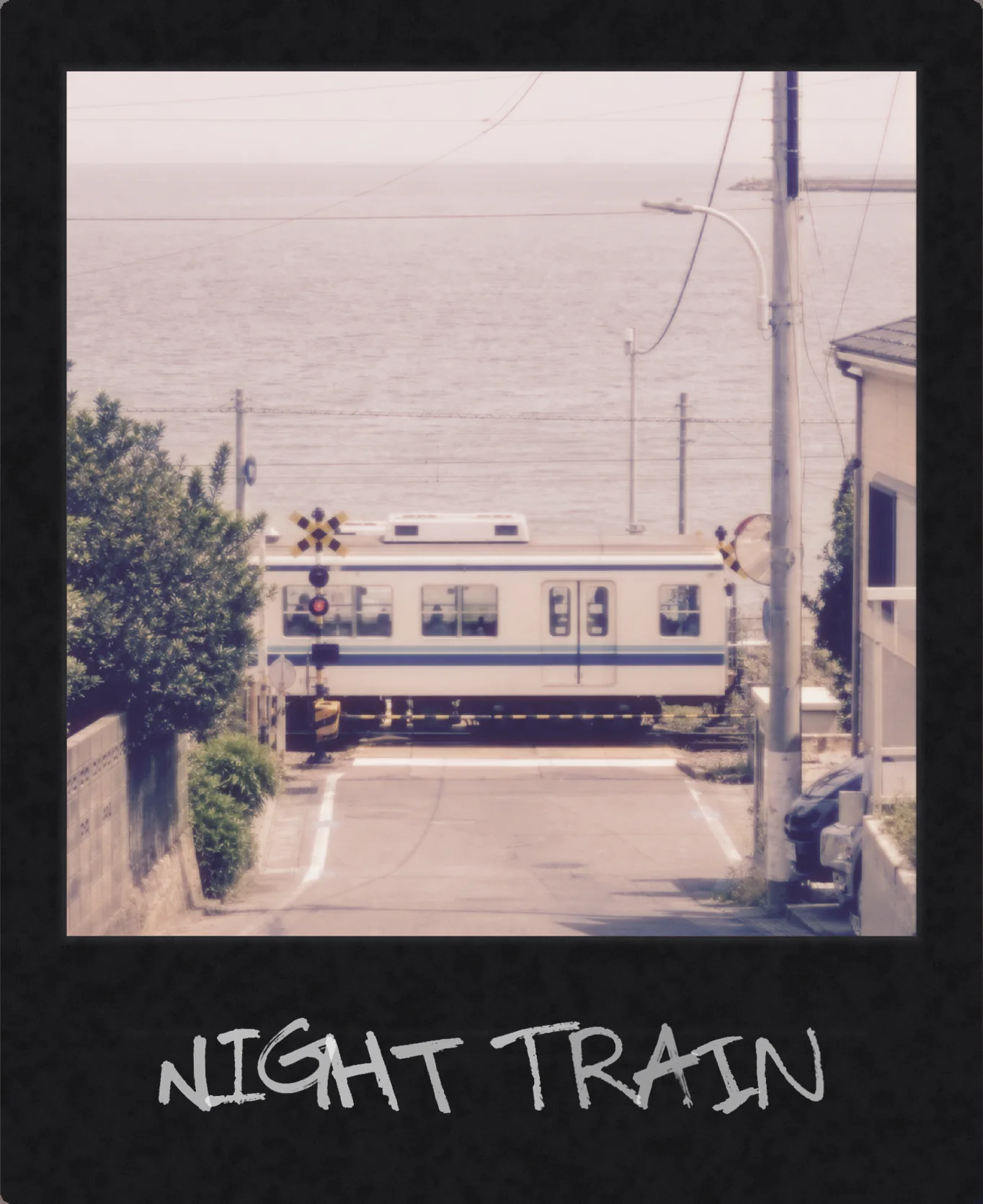 A seaside train crossing in a black instant frame with white handwriting