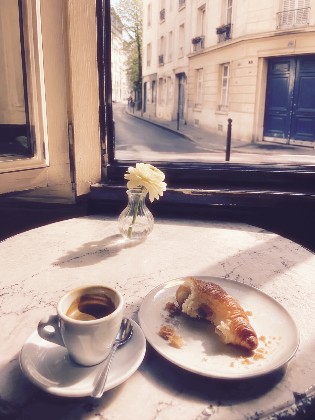 An AI-created café still life with espresso, a croissant and a flower, rendered in soft instant-film color
