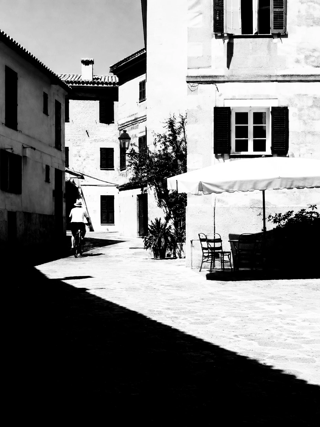 An AI-created village square with a cyclist and long shadows, rendered in high-contrast black and white
